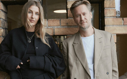 Fotografiskt dubbelporträtt av en kvinna och en man som står framför en tegelvägg.