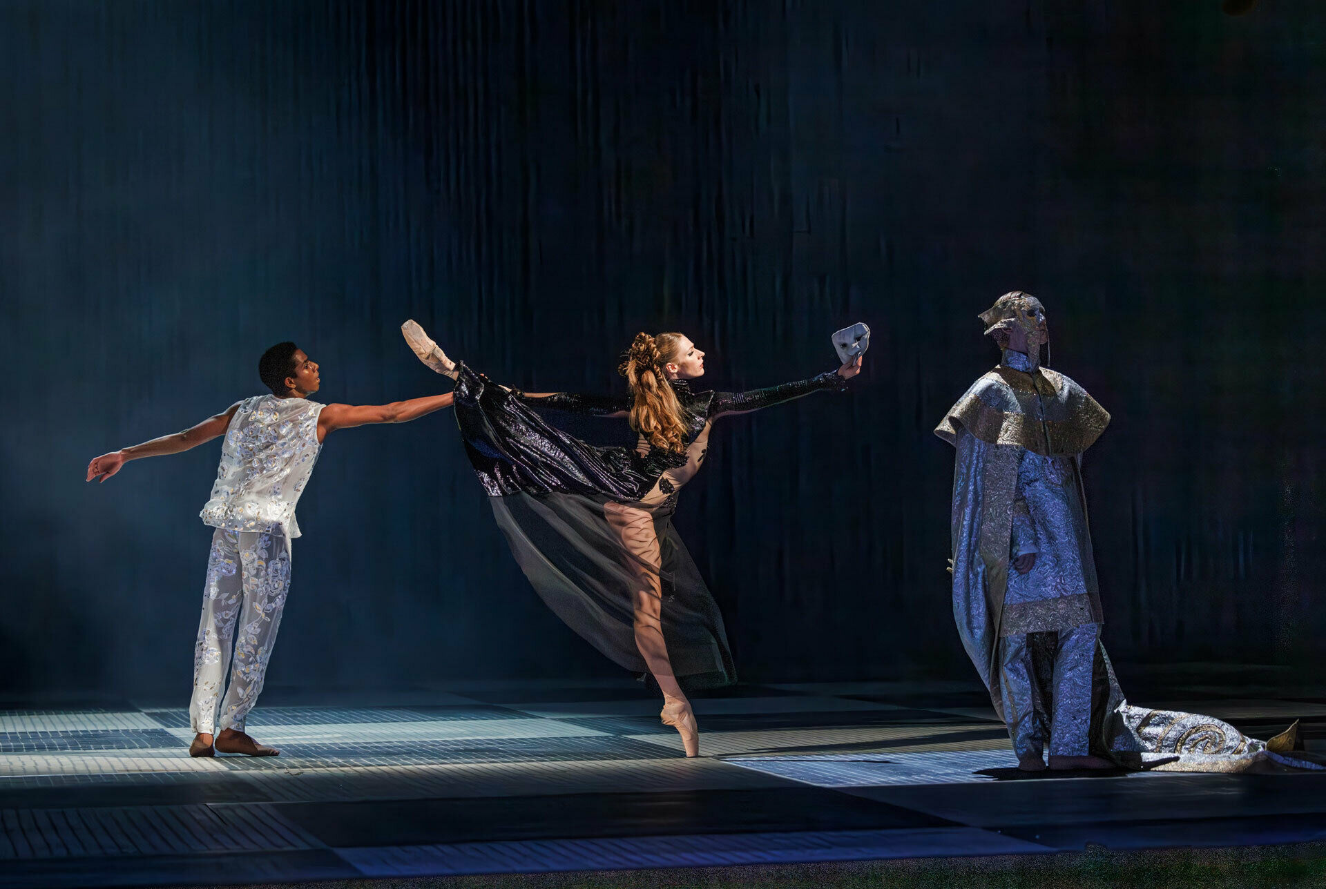 Foto från en scen i Kungliga Operans balett Gustavia. Tre personer i extravaganta dräkter.