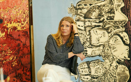 Fotografiskt porträtt av en kvinna - konstnären Karin Mamma Andersson - som sitter bland målningar i en ateljé