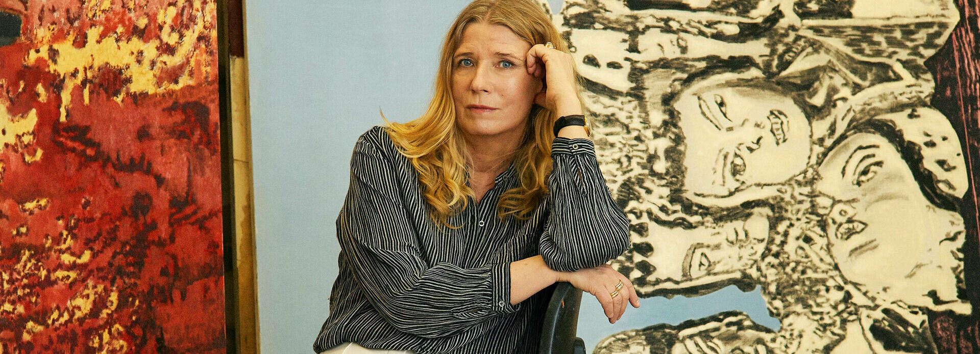 Fotografiskt porträtt av en kvinna - konstnären Karin Mamma Andersson - som sitter bland målningar i en ateljé